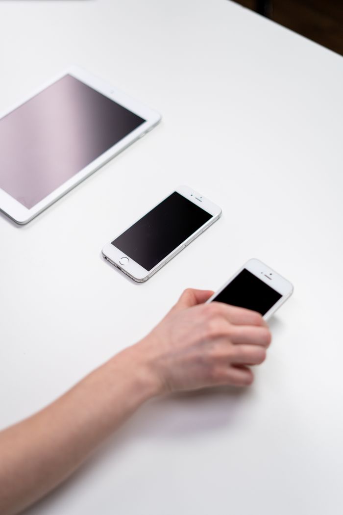 Overhead view of smartphones and a tablet on a white table with a hand reaching out.